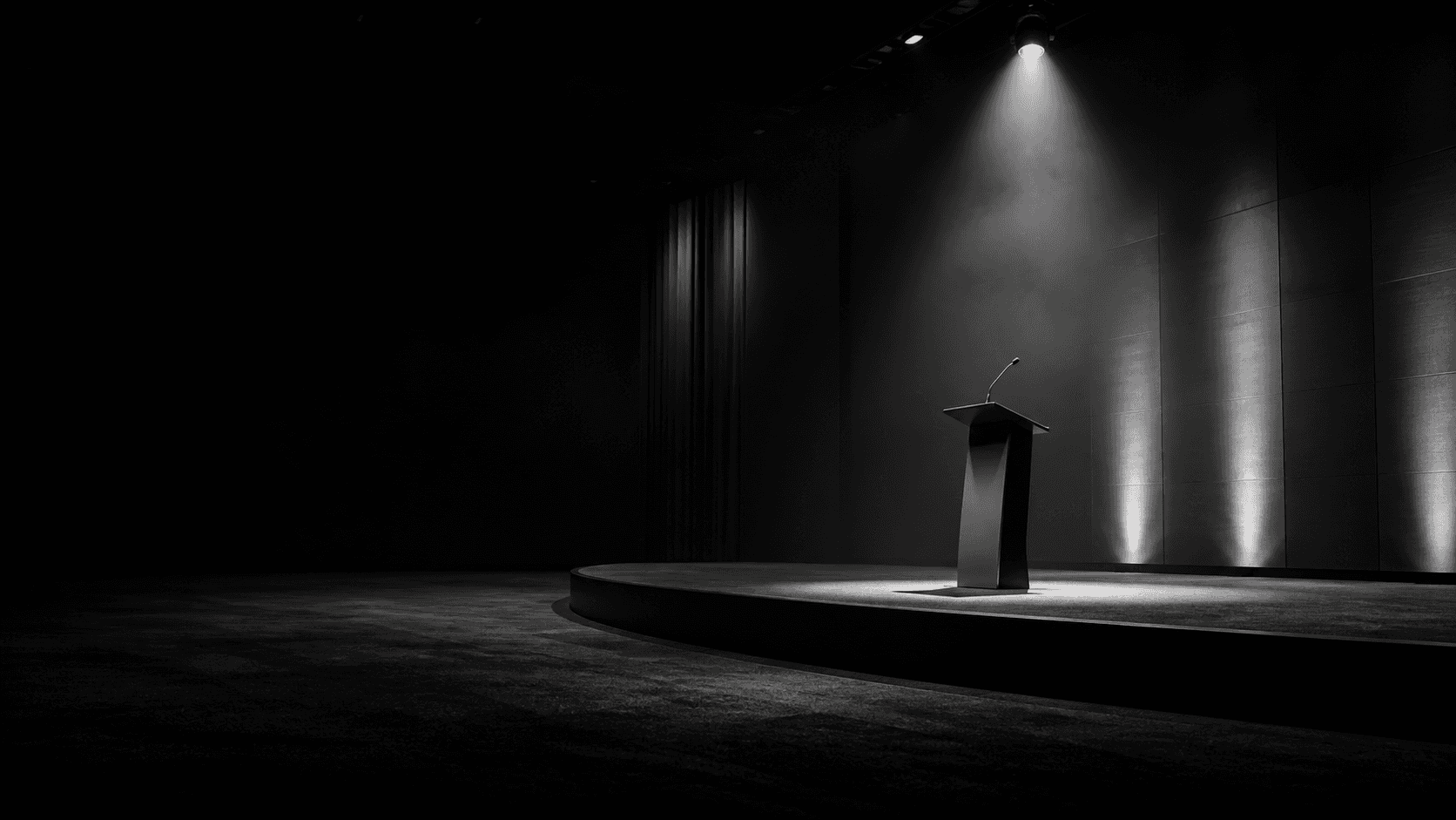 Black-and-white speaking stage with a podium under a spotlight.